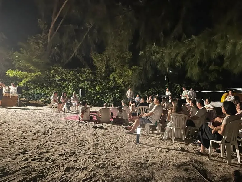 At night on a beach, a group of founders sit on chairs and on the sand, listening to a talk at the front