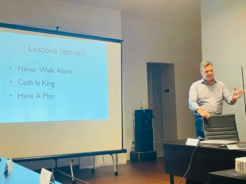 At a NEXEA session, Harald Weinbrecht stands next to a projector screen that reads Lessons learned: Never Walk Alone, Cash Is King, Have A Plan