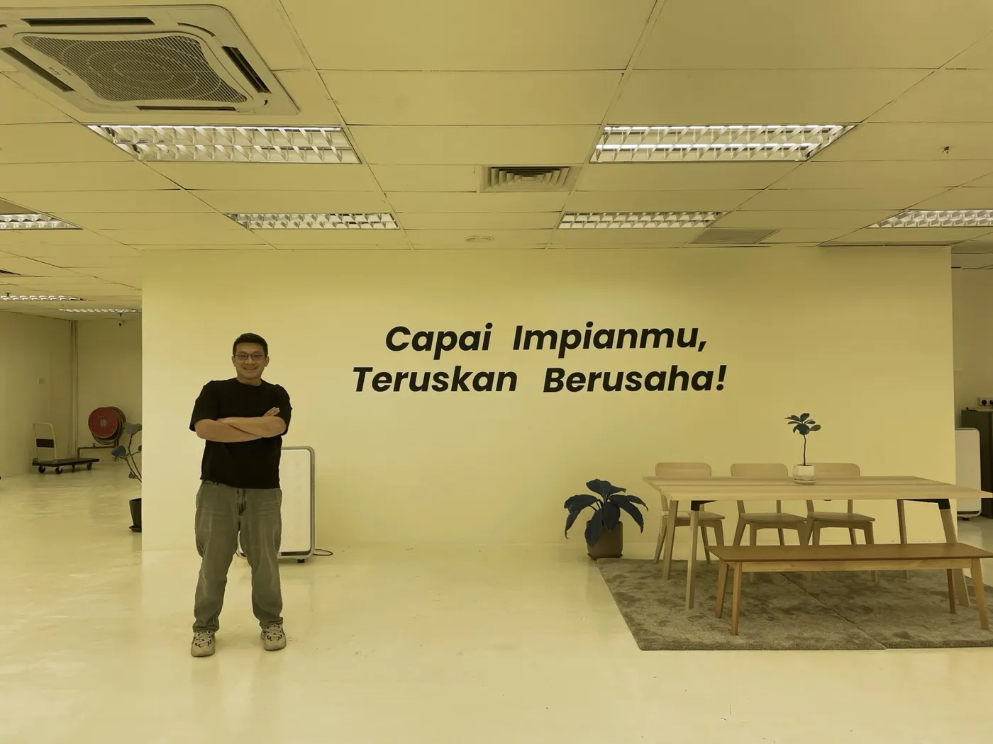 Gary standing in front of the office wall that reads Capai Impianmu, Teruskan Berusaha!