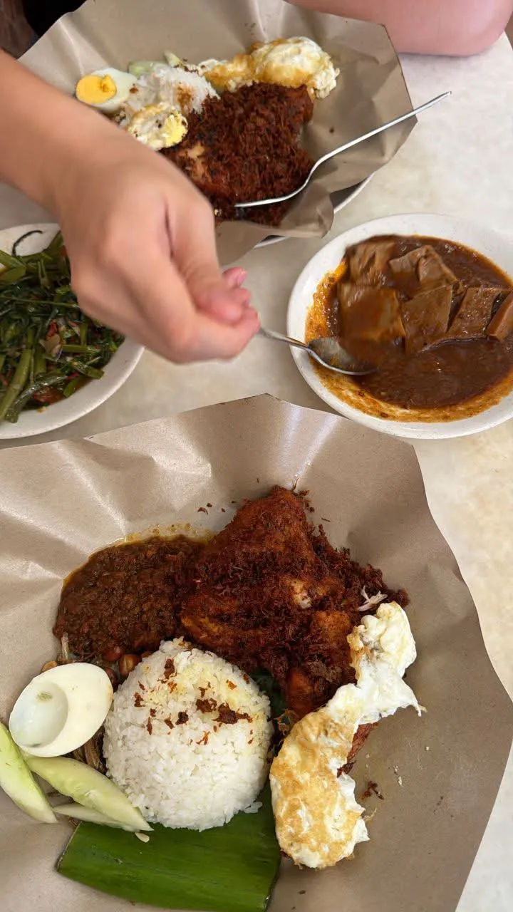 Village Park 的 nasi lemak:香饭、炸鸡上铺满香料碎、荷包蛋、半个水煮蛋、黄瓜和花生,旁边还有一盘 kangkung 和一碗咖喱