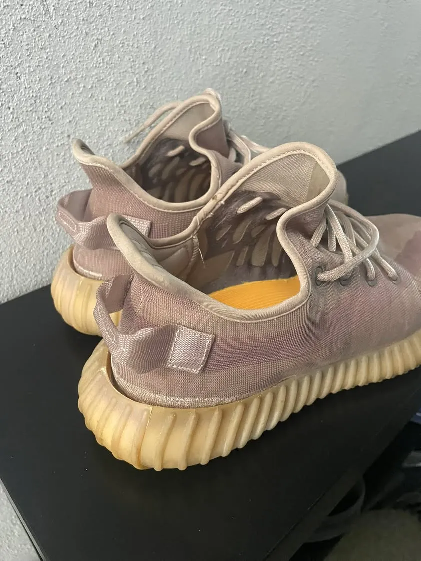 一双穿旧的 Yeezy 球鞋放在黑色桌面上,鞋身褪色发皱,鞋底已经发黄,后跟处开裂