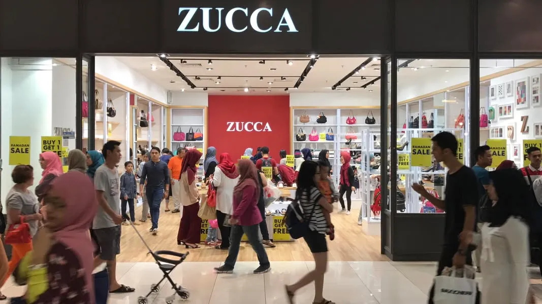 ZUCCA 实体店门口,店里挂满手袋,门口贴着 Ramadan Sale 和 Buy 1 Get 1 Free 的黄色海报,商场走廊人来人往